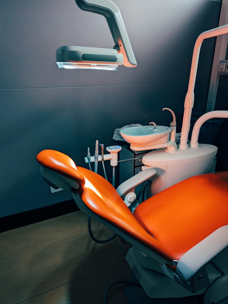 An orange dental chair with its instrument tray in a clinic room