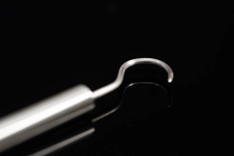 A dentist's metal explorer tool with a curved tip, on a dark surface