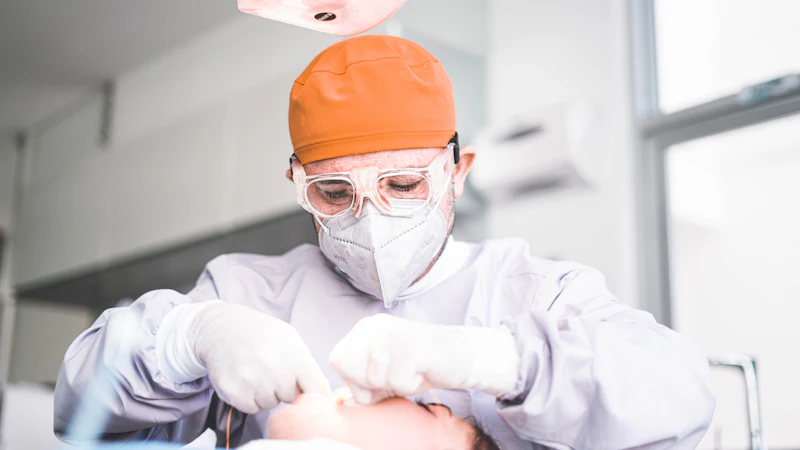 A dentist in an orange cap and safety glasses treating a patient